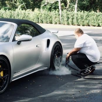Detailer steam-cleaning the wheel area of a silver sports car