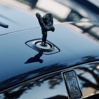 Glossy black Rolls-Royce hood reflecting nearby trees