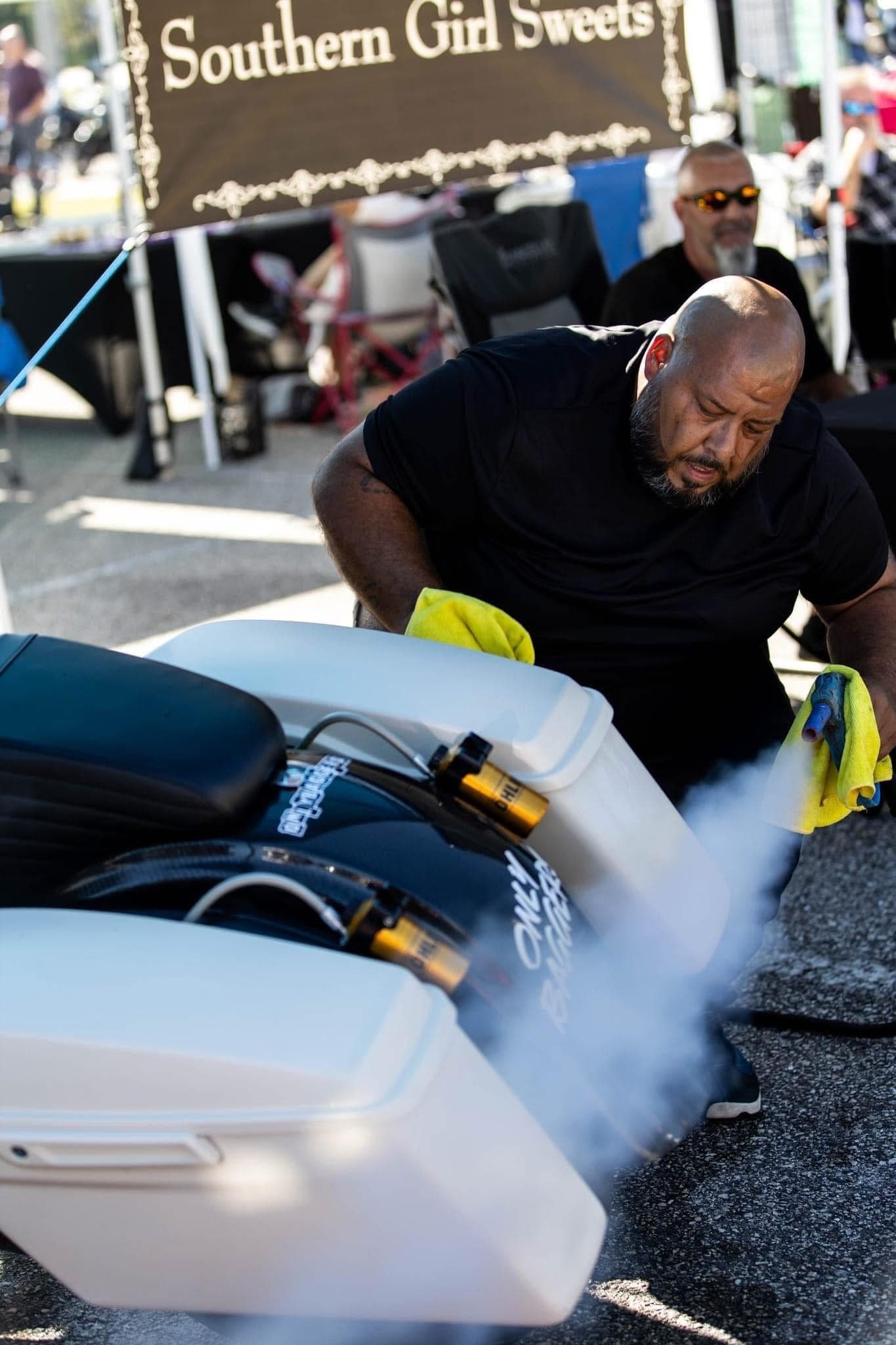 Detailer working on a white custom motorcycle at an outdoor event